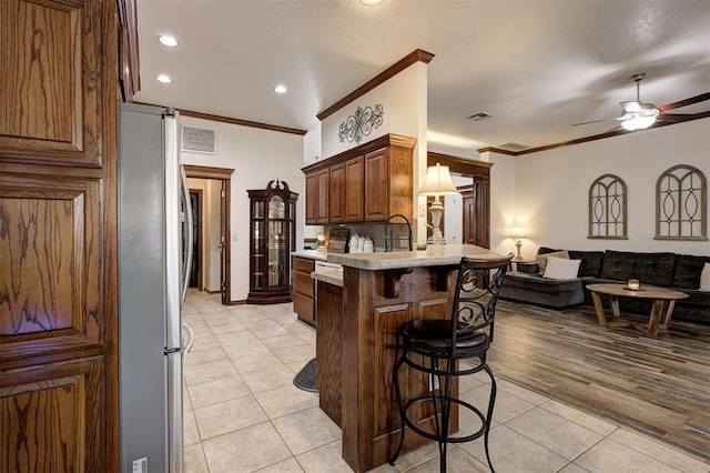 10633 NW 38th St, Yukon, OK 73099 - kitchen featuring freestanding refrigerator, a breakfast bar area, light tile patterned floors, a peninsula, and crown molding