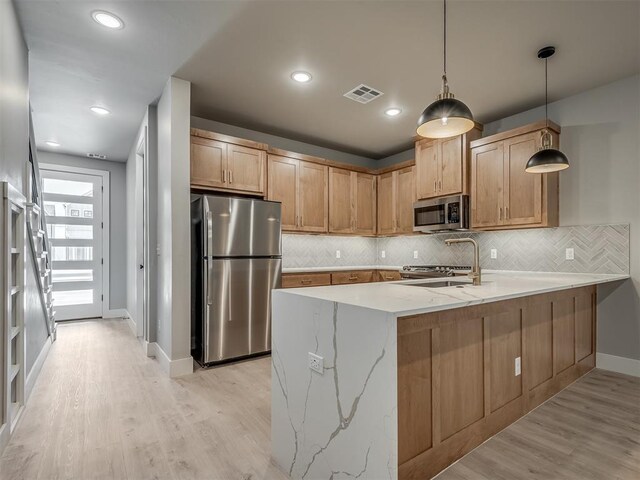 609 W 2nd St, Edmond, OK 73003 - kitchen with stainless steel appliances, a peninsula, decorative backsplash, light stone counters, and light wood-style flooring