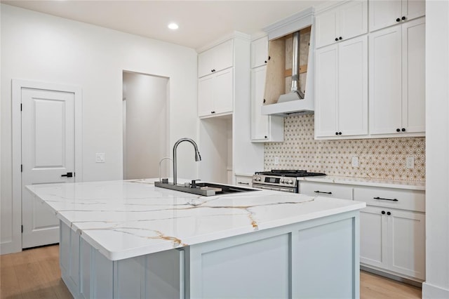 2705 NW 40th St, Oklahoma City, OK 73112 - kitchen featuring stainless steel range with gas cooktop, a kitchen island with sink, decorative backsplash, light wood finished floors, and recessed lighting
