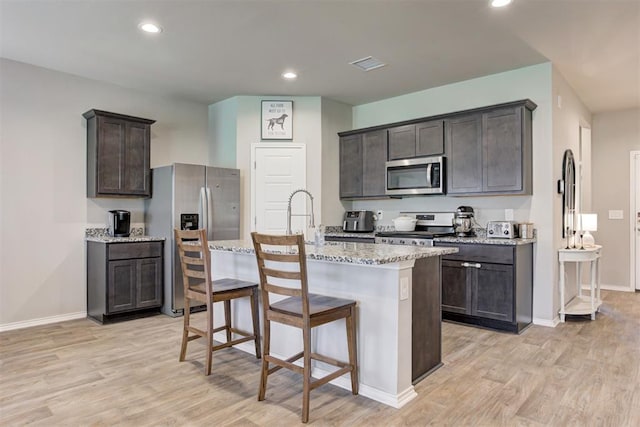 10409 NW 25th St, Yukon, OK 73099 - kitchen featuring stainless steel appliances, light wood-type flooring, dark brown cabinets, light stone countertops, and recessed lighting