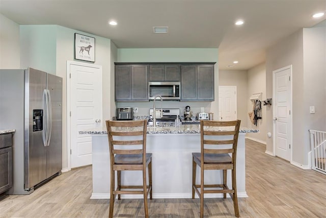 10409 NW 25th St, Yukon, OK 73099 - kitchen with stainless steel appliances, light wood finished floors, a kitchen breakfast bar, an island with sink, and light stone counters
