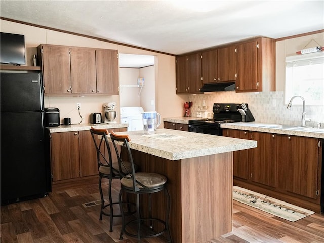 16940 Wildwood Dr, Lexington, OK 73051 - kitchen with black appliances, under cabinet range hood, dark wood-style flooring, light countertops, and washer and clothes dryer