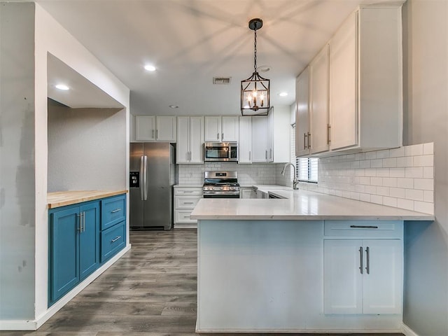2004 Tanglewood Dr, Edmond, OK 73013 - kitchen featuring stainless steel appliances, blue cabinetry, decorative backsplash, dark wood-style floors, and a peninsula