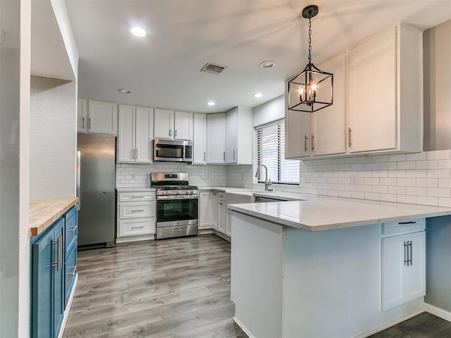2004 Tanglewood Dr, Edmond, OK 73013 - kitchen featuring appliances with stainless steel finishes, blue cabinets, a peninsula, light countertops, and light wood finished floors