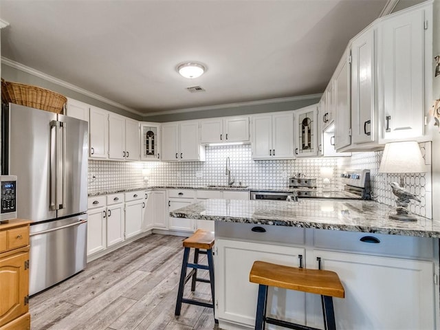 1616 E Cottonwood Rd, Goldsby, OK 73093 - kitchen featuring appliances with stainless steel finishes, a peninsula, light wood-type flooring, light stone countertops, and glass insert cabinets