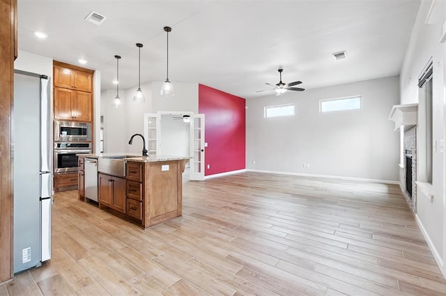 9233 NW 91st St, Yukon, OK 73099 - kitchen featuring a ceiling fan, appliances with stainless steel finishes, brown cabinets, a fireplace, and light wood finished floors