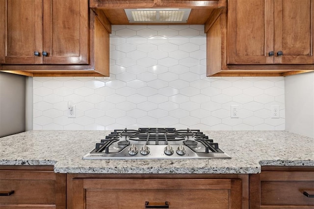 9233 NW 91st St, Yukon, OK 73099 - kitchen with stainless steel gas stovetop, exhaust hood, brown cabinets, decorative backsplash, and light stone countertops