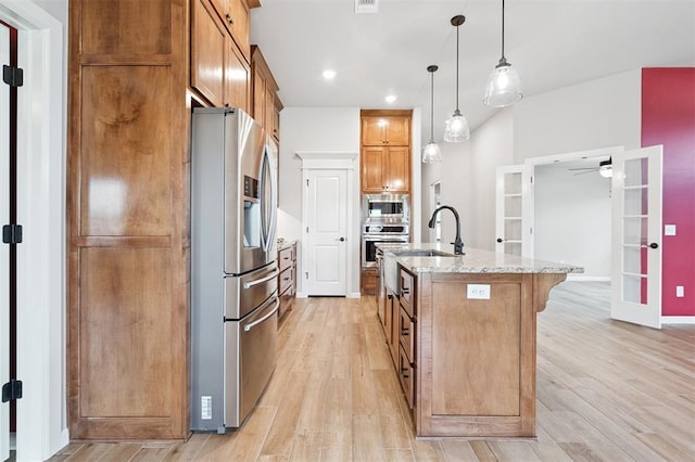 9233 NW 91st St, Yukon, OK 73099 - kitchen featuring appliances with stainless steel finishes, brown cabinets, light stone counters, light wood-type flooring, and a kitchen breakfast bar
