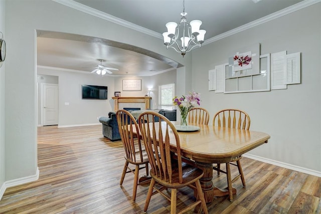 2209 Cedar Pointe Ct, Edmond, OK 73003 - dining area featuring wood finished floors, ceiling fan, crown molding, arched walkways, and a tiled fireplace
