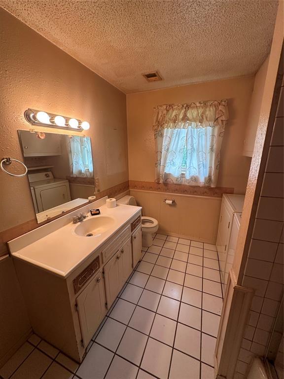 380 Weichel St, Colony, OK 73021 - bathroom featuring a textured ceiling, washer / clothes dryer, vanity, tile patterned floors, and a wainscoted wall