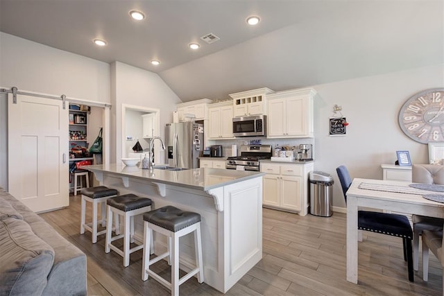 4004 Brougham Way, Oklahoma City, OK 73179 - kitchen with stainless steel appliances, vaulted ceiling, a breakfast bar, a kitchen island with sink, and a barn door
