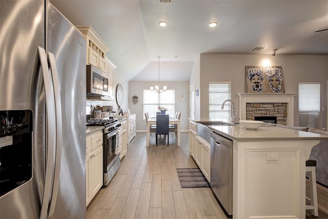 4004 Brougham Way, Oklahoma City, OK 73179 - kitchen featuring appliances with stainless steel finishes, a breakfast bar, a stone fireplace, a chandelier, and light wood finished floors