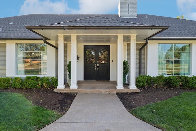 entrance to property with brick siding, roof with shingles, a porch, and a chimney