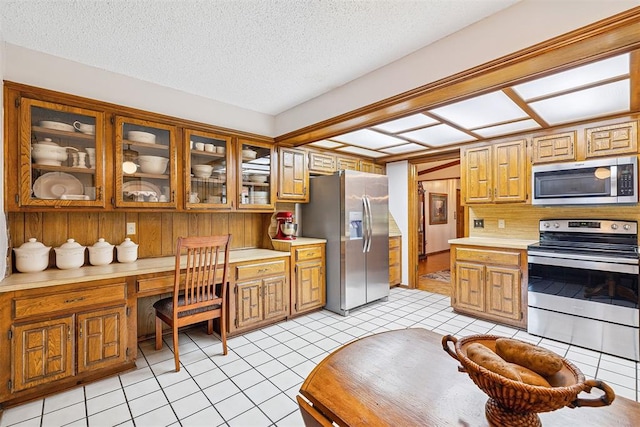 2408 Shady Tree Ln, Edmond, OK 73013 - kitchen with stainless steel appliances, light countertops, built in desk, light tile patterned floors, and a textured ceiling