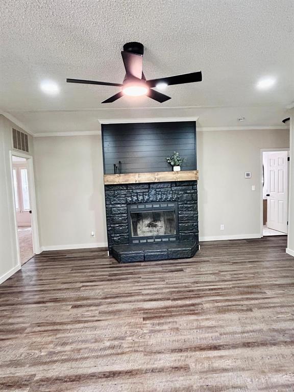 13001 Fox Pass Rd, Edmond, OK 73034 - unfurnished living room featuring a textured ceiling, wood finished floors, crown molding, ceiling fan, and a stone fireplace