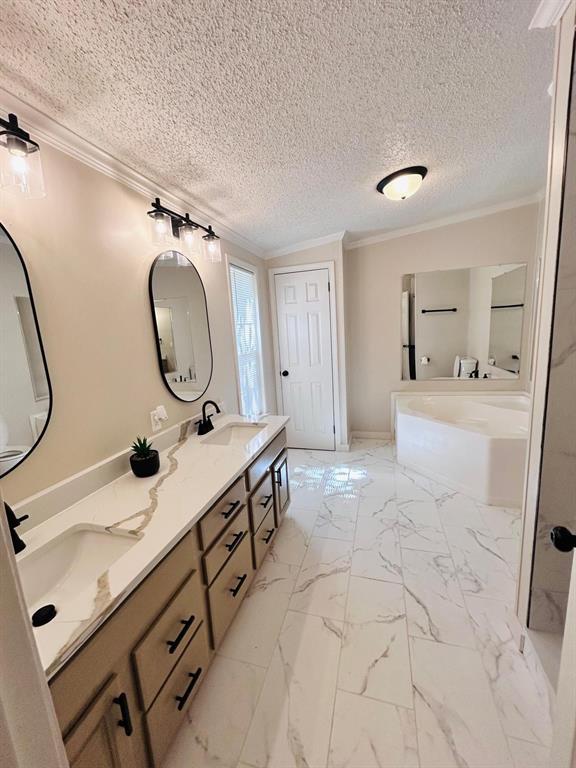 13001 Fox Pass Rd, Edmond, OK 73034 - bathroom with ornamental molding, a garden tub, double vanity, marble finish flooring, and a textured ceiling
