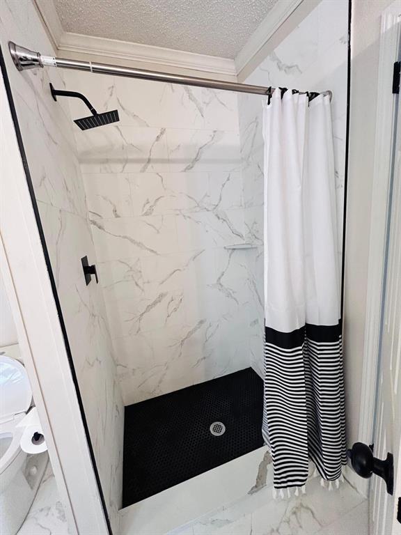 13001 Fox Pass Rd, Edmond, OK 73034 - bathroom with marble look tile flooring, ornamental molding, a textured ceiling, and a marble finish shower