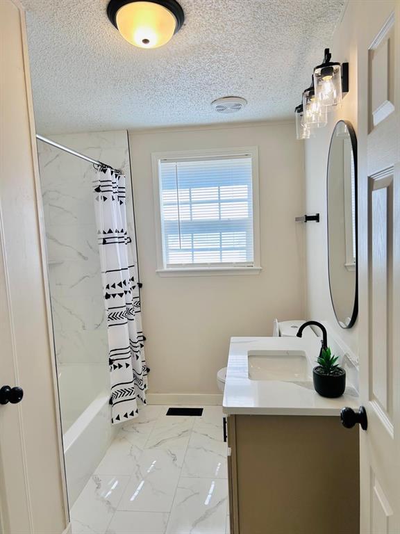 13001 Fox Pass Rd, Edmond, OK 73034 - bathroom featuring vanity, a textured ceiling, marble look tile flooring, and shower / bathtub combination with curtain