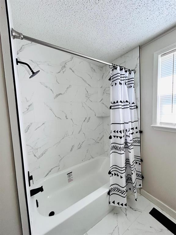 13001 Fox Pass Rd, Edmond, OK 73034 - full bath with a textured ceiling, shower / bathtub combination with curtain, and marble look tiles