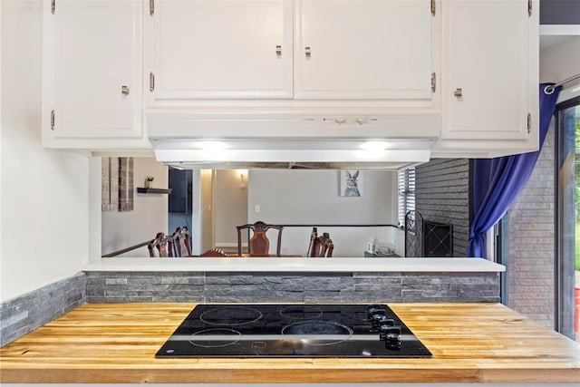 8316 NW 39th St, Bethany, OK 73008 - kitchen with black electric stovetop, under cabinet range hood, white cabinetry, a fireplace, and wooden counters