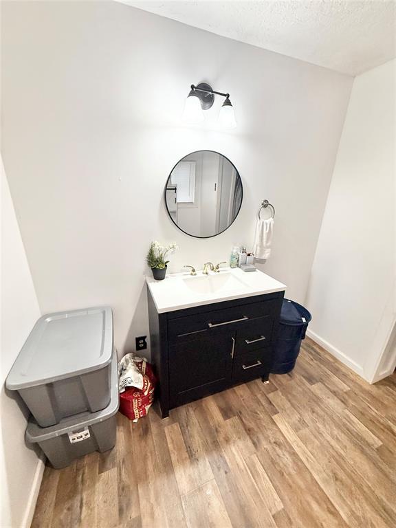 717 E Walnut St, Altus, OK 73521 - bathroom featuring wood finished floors, vanity, and a textured ceiling