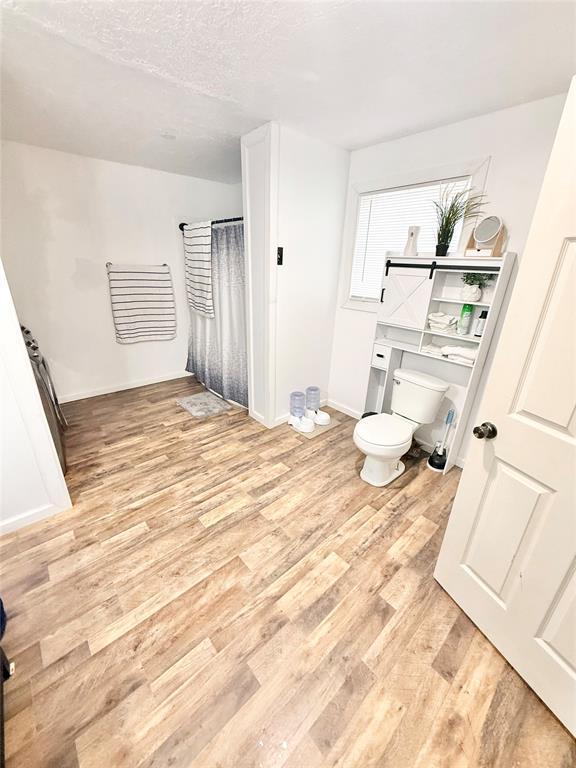 717 E Walnut St, Altus, OK 73521 - full bathroom with wood finished floors, a shower with curtain, and a textured ceiling