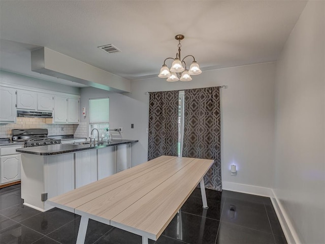 1713 SE 14th St, Moore, OK 73160 - kitchen with gas stove, under cabinet range hood, white cabinets, a chandelier, and backsplash