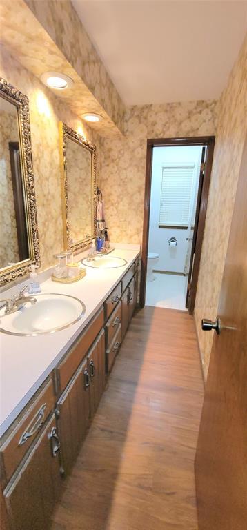 1117 Moose St, Yukon, OK 73099 - bathroom featuring double vanity, wood finished floors, and wallpapered walls