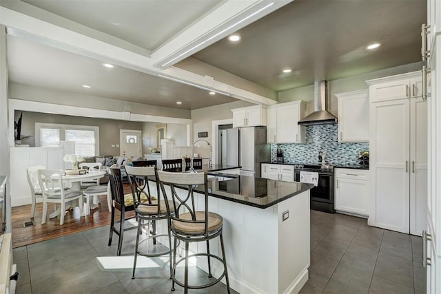 2233 W Eubanks St, Oklahoma City, OK 73112 - kitchen with wall chimney range hood, appliances with stainless steel finishes, a breakfast bar, dark tile patterned floors, and dark countertops