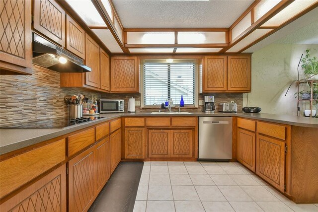 3121 SW 128th St, Oklahoma City, OK 73170 - kitchen with appliances with stainless steel finishes, under cabinet range hood, decorative backsplash, brown cabinetry, and a textured ceiling