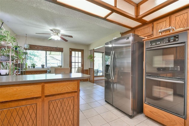 3121 SW 128th St, Oklahoma City, OK 73170 - kitchen featuring stainless steel fridge, ceiling fan, light tile patterned flooring, brown cabinetry, and a textured ceiling