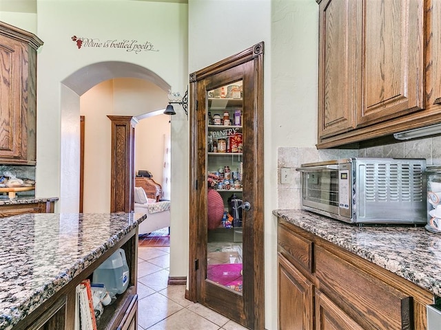 73 Sonata Ln, Shawnee, OK 74804 - kitchen featuring light tile patterned floors, arched walkways, dark stone counters, decorative backsplash, and brown cabinets
