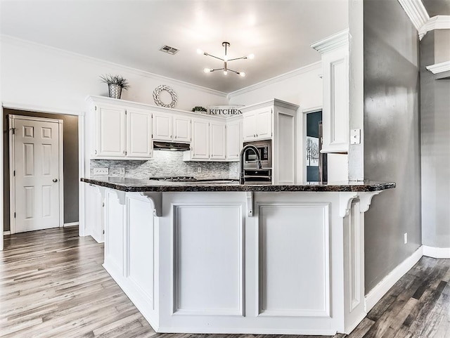 2044 Yorkshire Dr, Midwest City, OK 73130 - kitchen with under cabinet range hood, dark stone countertops, white cabinetry, light wood-type flooring, and backsplash