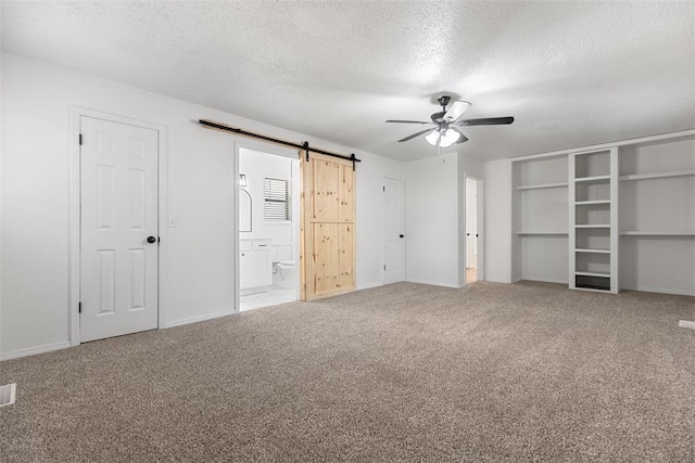 9617 Georgia Ave, Oklahoma City, OK 73120 - unfurnished bedroom featuring a barn door, a textured ceiling, carpet flooring, ensuite bathroom, and a ceiling fan