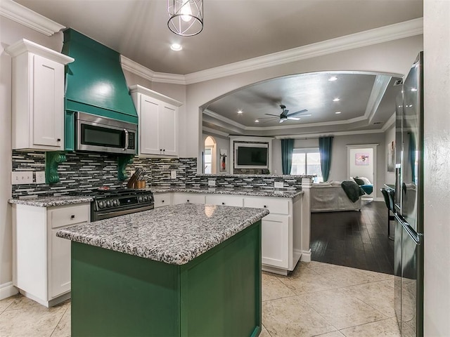 7032 NW 159th Pl, Edmond, OK 73013 - kitchen with stainless steel appliances, a ceiling fan, a peninsula, white cabinetry, and crown molding