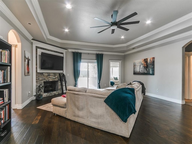 7032 NW 159th Pl, Edmond, OK 73013 - living area featuring ceiling fan, arched walkways, a stone fireplace, a tray ceiling, and dark wood finished floors
