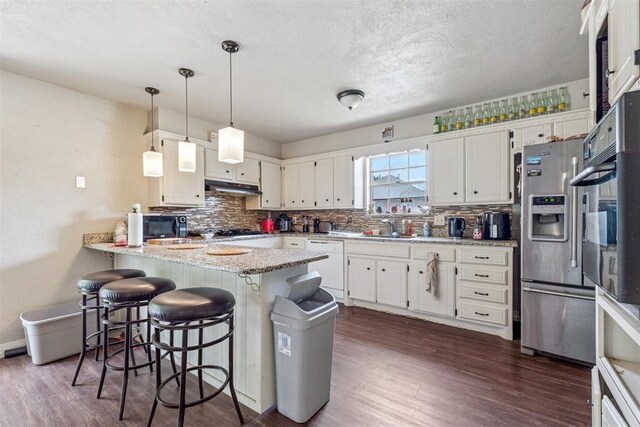 11900 Surrey Ln, Yukon, OK 73099 - kitchen featuring white dishwasher, under cabinet range hood, a peninsula, dark wood finished floors, and backsplash