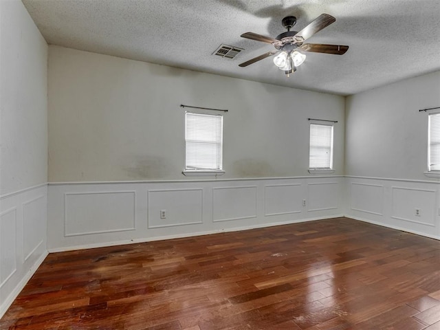 4113 Clendon Way, Del City, OK 73115 - empty room featuring plenty of natural light, hardwood / wood-style flooring, a ceiling fan, a textured ceiling, and a wainscoted wall