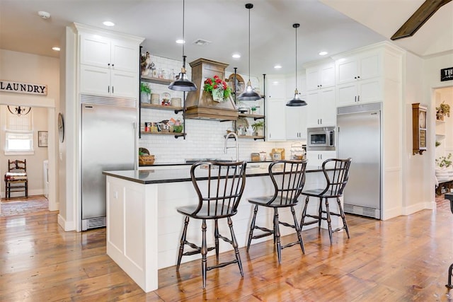 209 Pont Julienn Ct, Edmond, OK 73034 - kitchen with built in appliances, open shelves, backsplash, dark countertops, and a breakfast bar area