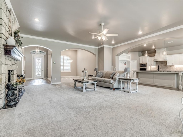 210 Bulverde Dr, Norman, OK 73069 - living area featuring light carpet, crown molding, a ceiling fan, arched walkways, and a stone fireplace