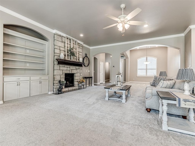 210 Bulverde Dr, Norman, OK 73069 - carpeted living room featuring crown molding, ceiling fan, arched walkways, a stone fireplace, and built in shelves