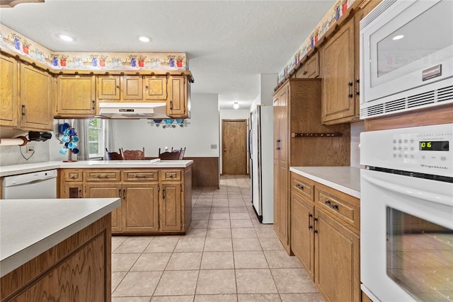 717 Maple St, Weatherford, OK 73096 - kitchen with white appliances, under cabinet range hood, light countertops, brown cabinetry, and light tile patterned floors