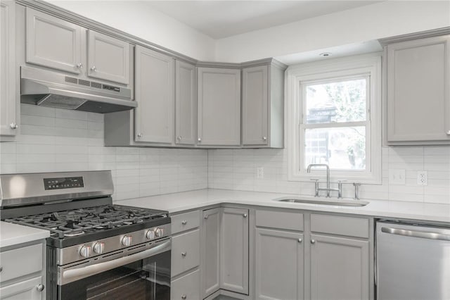 933 SW 50th St, Oklahoma City, OK 73109 - kitchen featuring stainless steel appliances, under cabinet range hood, gray cabinetry, light countertops, and backsplash