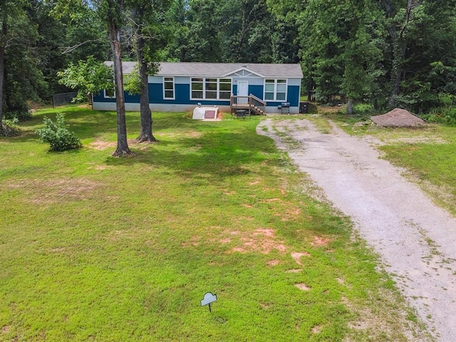 view of front of property featuring driveway, a front yard, and a view of trees