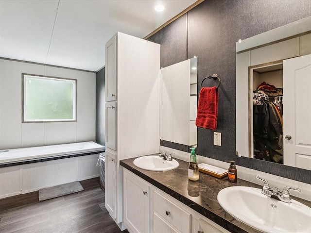 bathroom featuring double vanity, wood finished floors, a spacious closet, and a tub to relax in