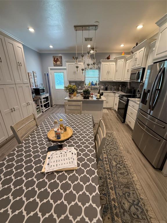 105967 S Rolling Hills Dr, Meeker, OK 74855 - kitchen featuring appliances with stainless steel finishes, light wood-type flooring, tasteful backsplash, a center island, and white cabinets