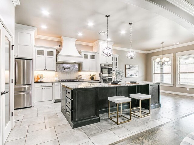 3009 Cordova Ct, Norman, OK 73072 - kitchen featuring custom range hood, appliances with stainless steel finishes, decorative backsplash, an island with sink, and white cabinets
