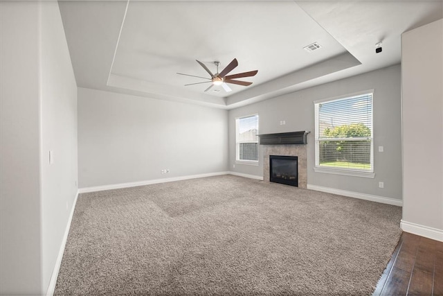 8309 NW 139th Ter, Oklahoma City, OK 73142 - unfurnished living room with a tray ceiling, a ceiling fan, a tiled fireplace, dark wood finished floors, and dark carpet