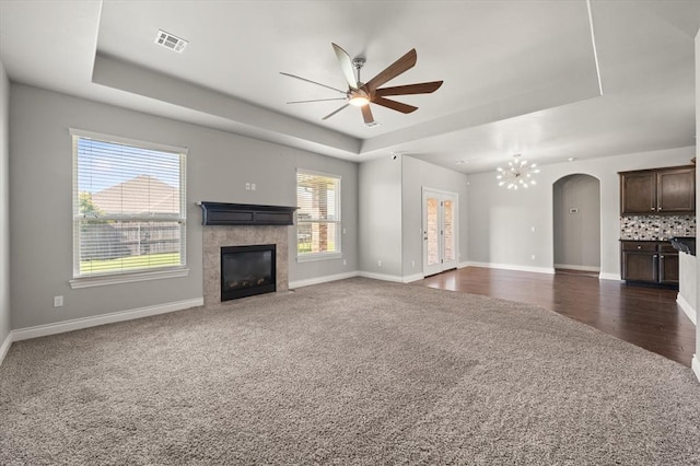 8309 NW 139th Ter, Oklahoma City, OK 73142 - unfurnished living room with a tray ceiling, a fireplace, dark colored carpet, a ceiling fan, and a chandelier