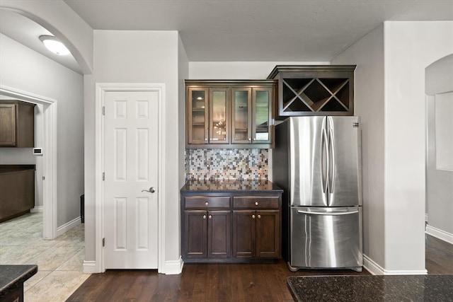 8309 NW 139th Ter, Oklahoma City, OK 73142 - kitchen featuring freestanding refrigerator, arched walkways, backsplash, glass insert cabinets, and dark brown cabinets